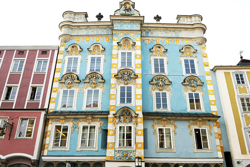 Ein Haus mit Erkern und verzierter blauer Fassade ragt auf. Steyr Oesterreich Stadtplatz