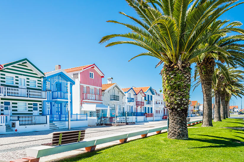 Entlang einer gepflasterten Promenade in Costa Nova reihen sich die berühmten „Palheiros“, farbenfroh gestreifte Holzhäuser in Grün, Blau und Rot mit Weiß. Top Tagestrips Porto Costa Nova