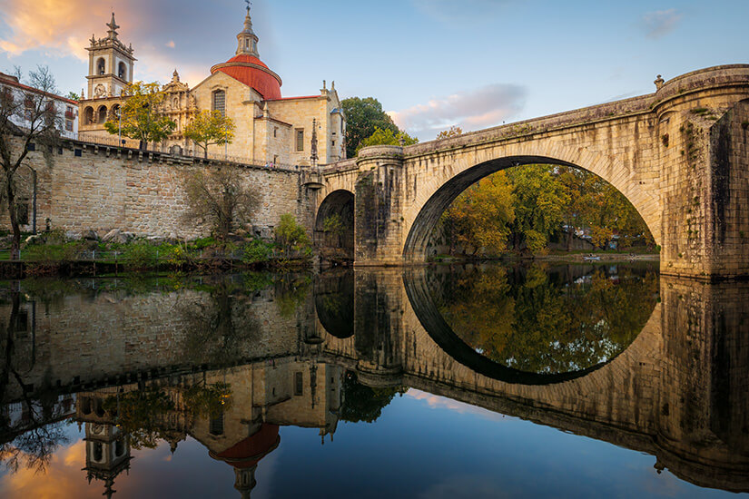 Über den spiegelglatten Fluss Tâmega in Amarante spannt sich die steinerne Ponte de São Gonçalo, deren großer Bogen sich im Wasser zu einem nahezu perfekten Kreis ergänzt. Top Tagestrips Porto Amarante