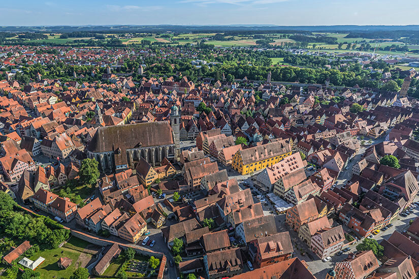 Die Stadt Dinkelsbühl von oben betrachtet. Eine Stadtmauer umgibt die Gebäude mit ihren roten Dächern. Im Hinterland liegt viel Grün. Dinkelsbuehl Deutschland Willkommen