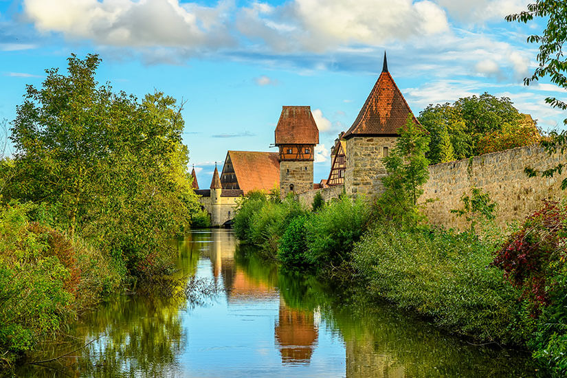 Der Fluss Wörnitz führt vorbei an grüner Landschaft sowie der Stadtmauer von Dinkelsbühl. Dinkelsbuehl Deutschland Stadtmauer