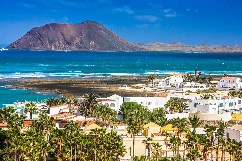 Corralejo auf Fuerteventura ist zu sehen. Grüne Palmen, weiße Häuser und blaues Meer mit Hügeln im Hintergrund prägen das Bild. All Inclusive unter 1000 Euro Fuerteventura
