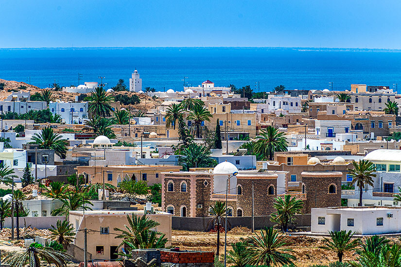 Die Stadt Djerba mit klassischer Architektur ist zu sehen. Dahinter liegt das blaue Meer. All Inclusive unter 1000 Euro Djerba
