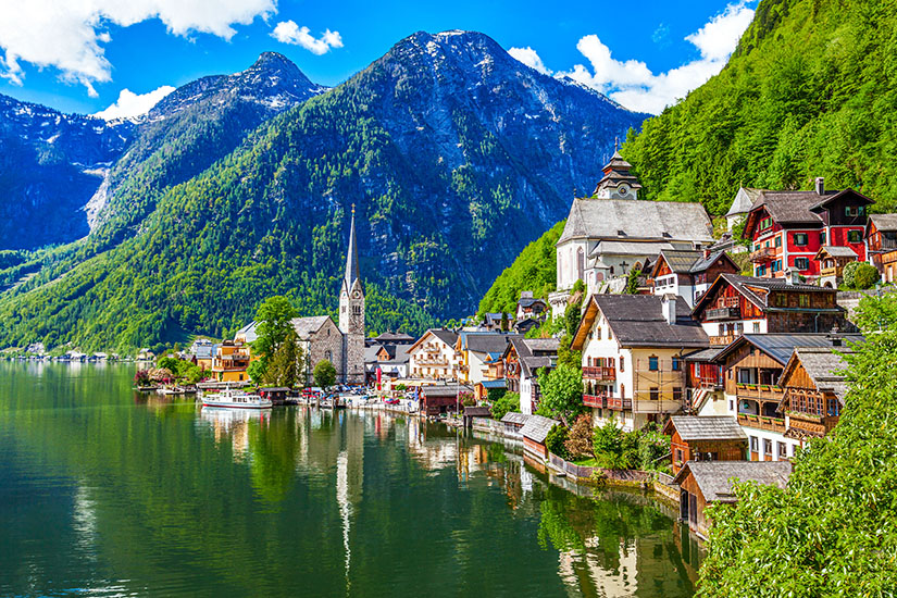 Zu erkennen ist Hallstatt am Hallstätter See, mit traditionellen Häusern und markanten Kirchtürmen direkt am Ufer. Im Hintergrund erheben sich steile, dicht bewaldete Berge und verleihen dem Ort eine eindrucksvolle alpine Kulisse. Oesterreich Hallstatt