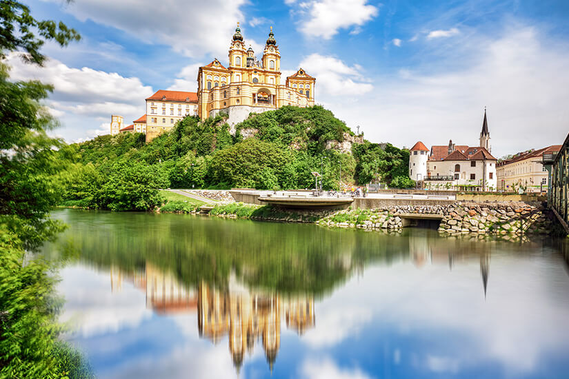 Zu erkennen ist das barocke Stift Melk, das auf einem bewaldeten Hügel über dem Wasser thront. Die prächtige Klosteranlage mit ihren markanten Türmen spiegelt sich eindrucksvoll in der ruhigen Wasseroberfläche. Oesterreich Melk