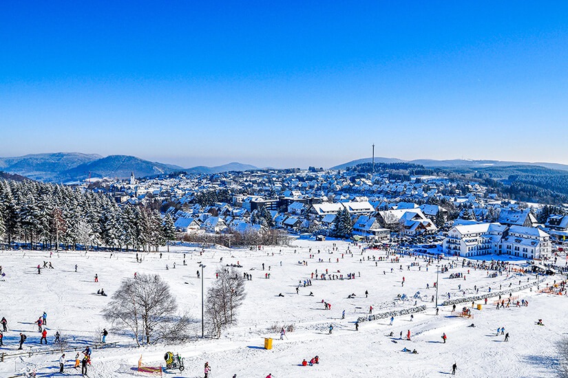 Das Skigebiet von Winterberg ist zu sehen. Zahlreiche Sportler tummeln sich im Schnee. Winterberg Sauerland Skifahren