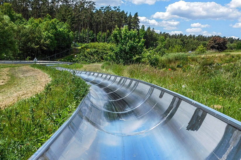Eine Sommerrodelbahn aus der Sicht eines Fahrers ist zu sehen. Sie verläuft durch grüne, sommerliche Landschaft. Winterberg Sauerland Sommerrodelbahn