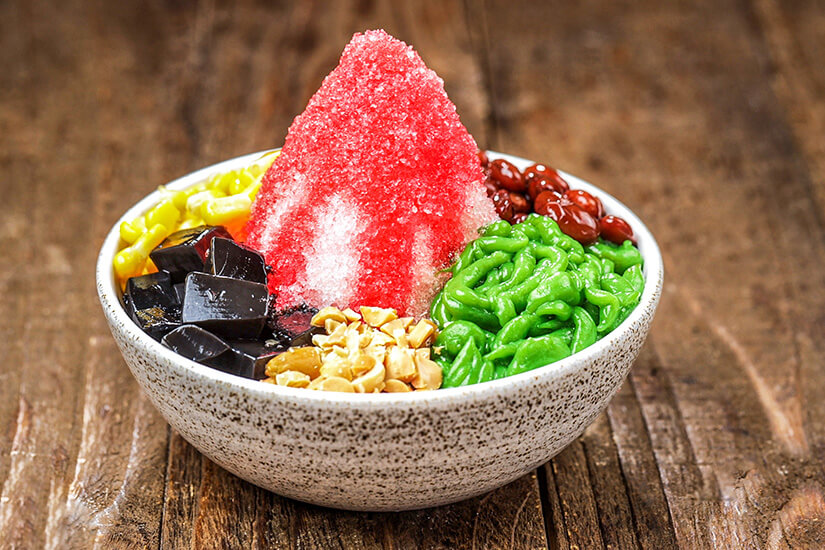 In einer gesprenkelten Keramikschale türmt sich Ais Kacang, ein malaysisches Dessert aus fein geschabtem Eis, das mit leuchtend rotem Sirup übergossen ist. Malaysisches Essen Ais Kacang