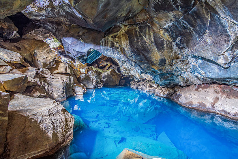 In der Lavahöhle Grjótagjá nahe dem Mývatn-See schimmert eine heiße Quelle in leuchtendem Türkisblau, umgeben von zerklüftetem, dunklem Vulkangestein. Game of Thrones Drehorte Island