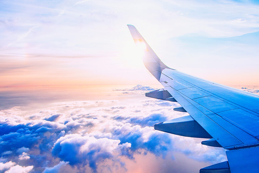 Aus dem Fenster eines Flugzeugs fällt der Blick auf die Tragfläche mit nach oben gebogenem Winglet, die hoch über einem flauschigen Wolkenmeer schwebt. Co2 Rechner Reisen Flugzeug