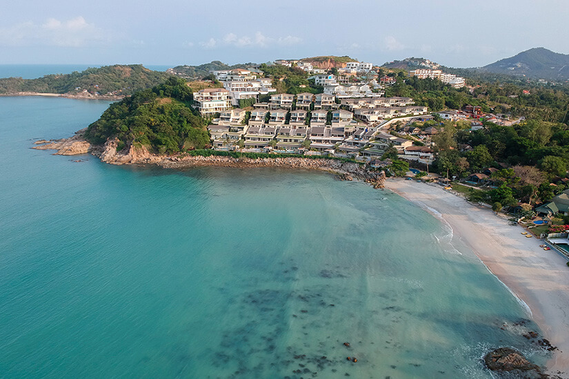 Weiße Resorts liegen an den grünen Hängen einer Insel. Davor befindet sich ein schmaler heller Strand mit glasklarem Wasser. White Lotus Drehorte Choeng Mon