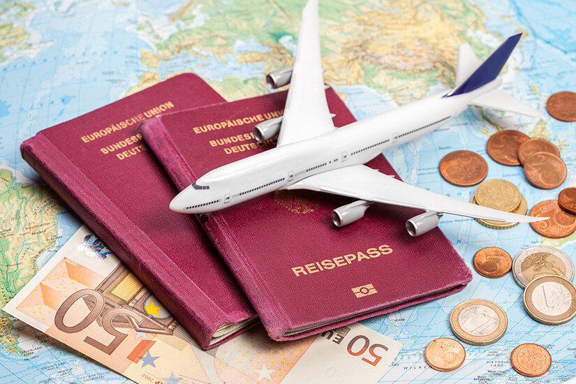 Ein weißes Modellflugzeug liegt zusammen mit zwei roten deutschen Reisepässen, mehreren Euro-Geldscheinen und Münzen auf einer ausgebreiteten Weltkarte. Pauschalreisen unter 500 Euro Zielgruppe