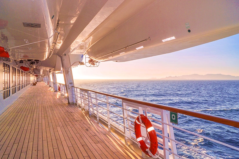 Holzdeck eines Kreuzfahrtschiffs mit Rettungsring und Blick auf das Meer im Abendlicht