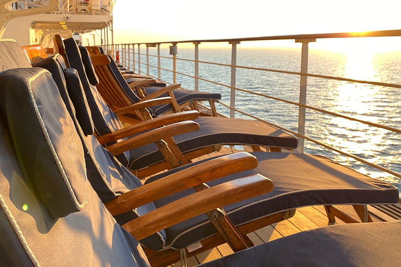 Reihe von Liegestühlen auf dem Deck eines Kreuzfahrtschiffs mit Blick aufs Meer im Sonnenuntergang